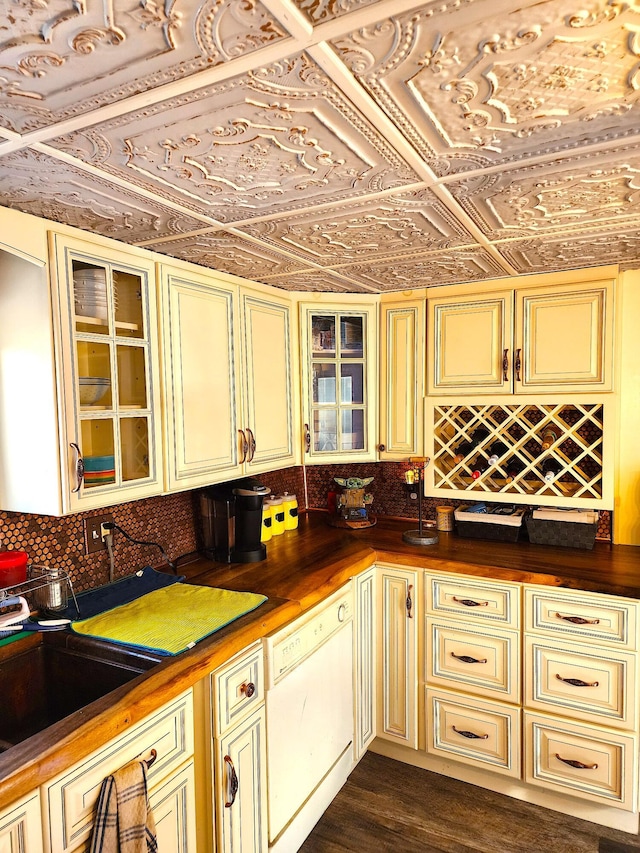 kitchen featuring dishwasher, an ornate ceiling, glass insert cabinets, cream cabinetry, and backsplash