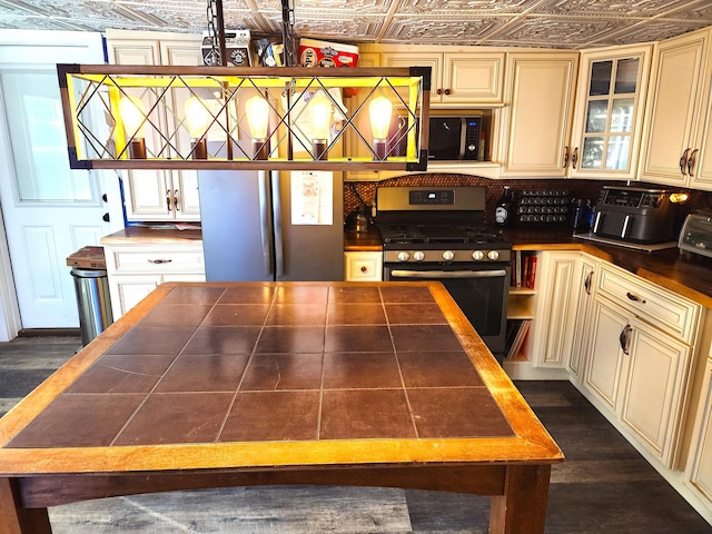 kitchen with tile countertops, an ornate ceiling, glass insert cabinets, appliances with stainless steel finishes, and cream cabinetry