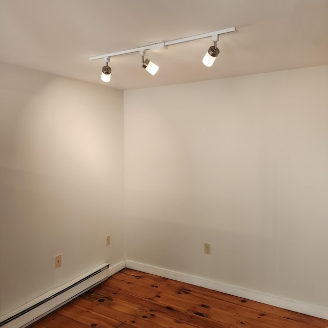 empty room featuring a baseboard heating unit, wood-type flooring, rail lighting, and baseboards