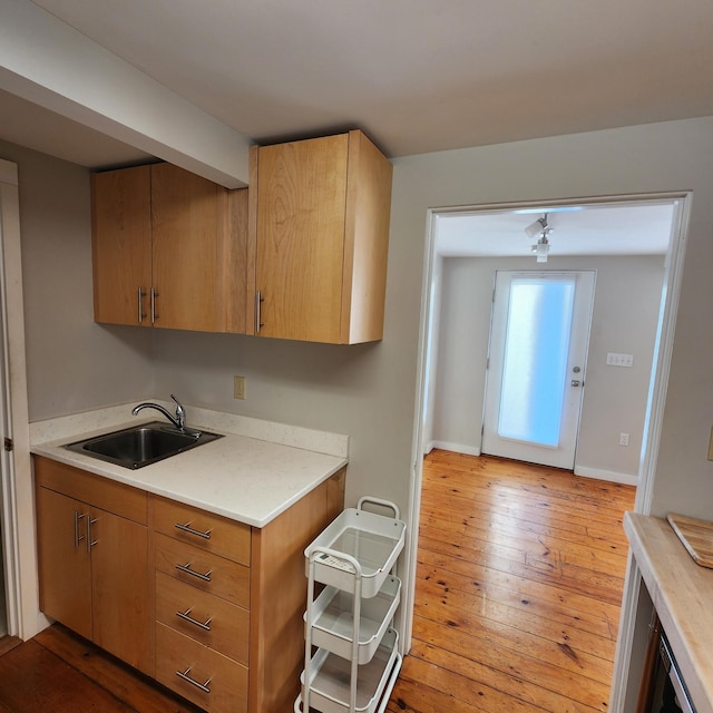 kitchen featuring light countertops, hardwood / wood-style floors, a sink, and baseboards