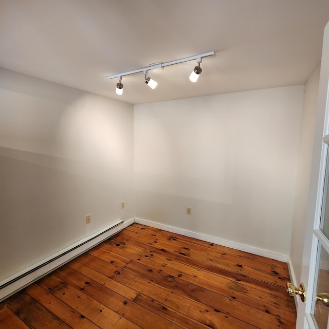 spare room featuring a baseboard heating unit, hardwood / wood-style flooring, and baseboards