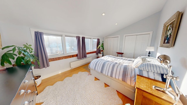 bedroom featuring baseboards, radiator, lofted ceiling, wood finished floors, and multiple closets