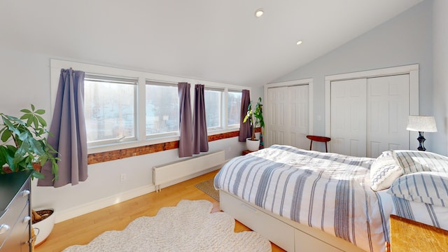 bedroom with baseboards, radiator heating unit, wood finished floors, vaulted ceiling, and two closets