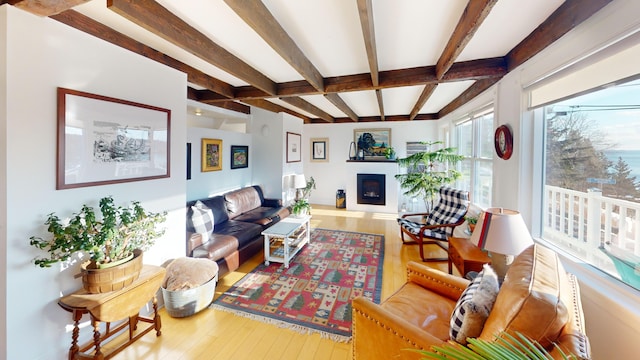 living area with beamed ceiling, hardwood / wood-style floors, and a glass covered fireplace