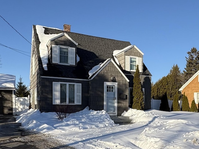 cape cod-style house featuring roof with shingles and a chimney