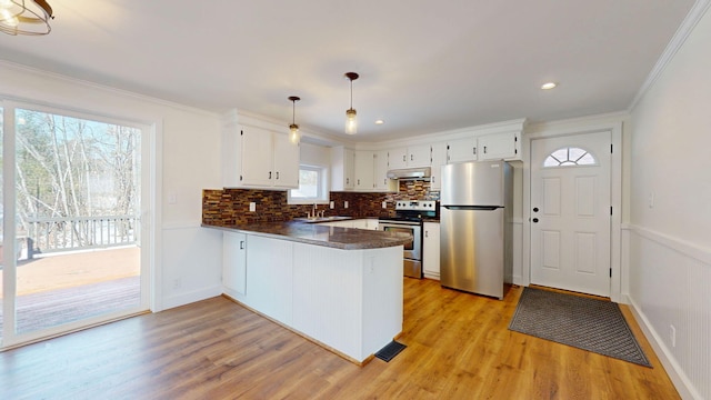 kitchen featuring a peninsula, appliances with stainless steel finishes, under cabinet range hood, white cabinetry, and dark countertops