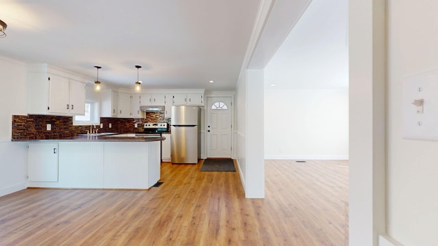 kitchen with under cabinet range hood, dark countertops, tasteful backsplash, appliances with stainless steel finishes, and a peninsula