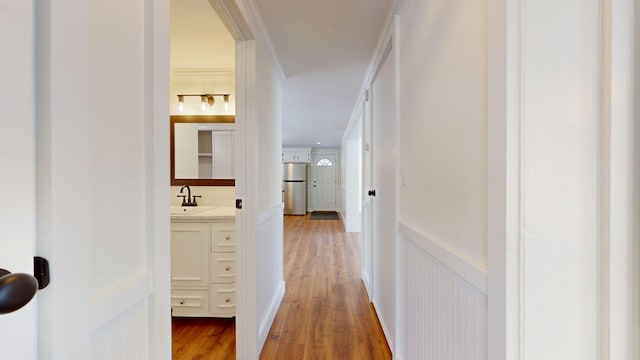 corridor featuring a wainscoted wall, light wood-style flooring, ornamental molding, a sink, and a decorative wall