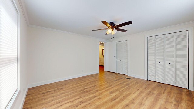 unfurnished bedroom with light wood-style flooring, multiple closets, baseboards, and ornamental molding