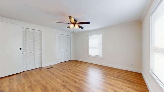 unfurnished bedroom featuring light wood finished floors, baseboards, crown molding, and multiple closets