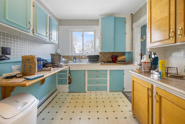 kitchen with backsplash, baseboard heating, light countertops, light floors, and a sink