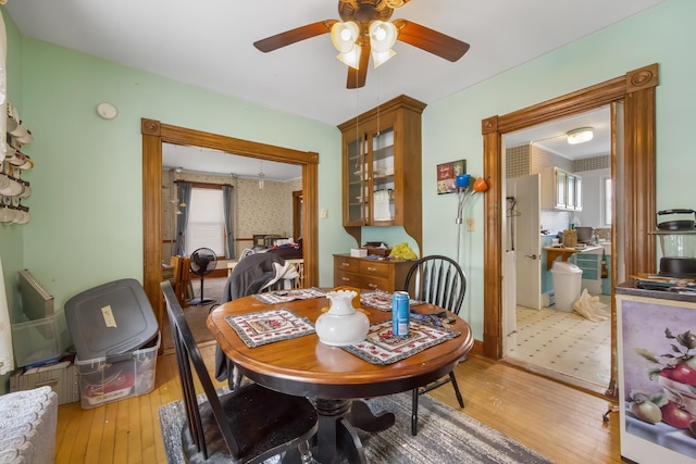 dining room with light wood-style floors, a ceiling fan, and wallpapered walls