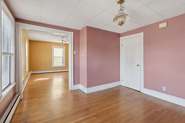 empty room featuring a baseboard heating unit, hardwood / wood-style flooring, baseboards, and a drop ceiling