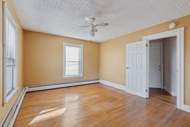 empty room featuring a ceiling fan, baseboards, a baseboard radiator, light wood-style flooring, and baseboard heating