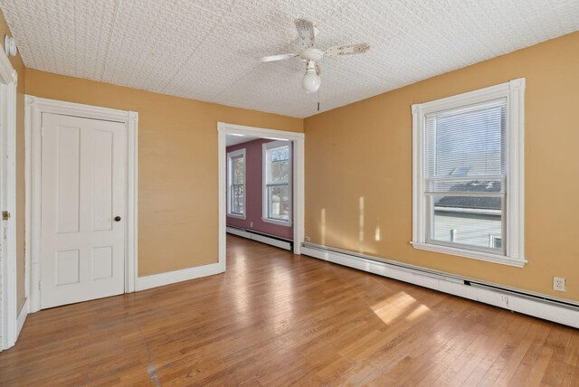 empty room featuring baseboards, wood-type flooring, a ceiling fan, and a baseboard radiator