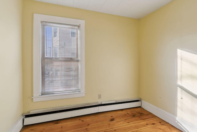 empty room with a baseboard heating unit, a healthy amount of sunlight, light wood-type flooring, and baseboards