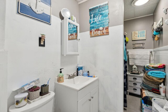 half bath featuring vanity, toilet, and a drop ceiling