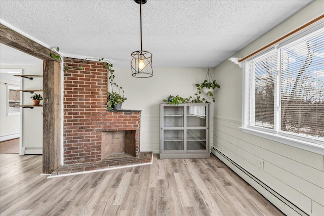 unfurnished living room featuring a textured ceiling, a baseboard heating unit, a wainscoted wall, wood finished floors, and a brick fireplace