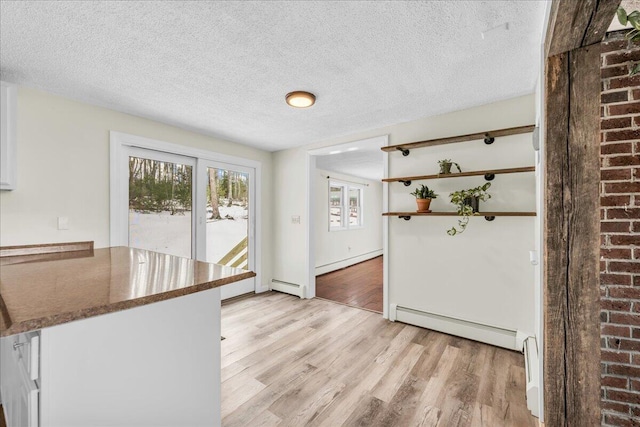 kitchen with dark countertops, a baseboard heating unit, light wood-style floors, white cabinetry, and a textured ceiling