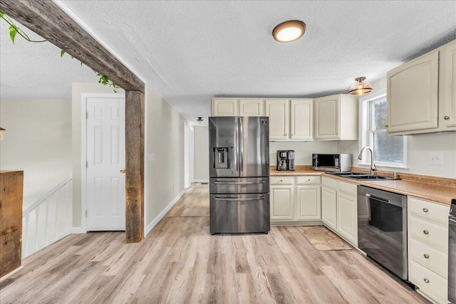 kitchen with stainless steel appliances, a textured ceiling, light countertops, light wood-type flooring, and a sink