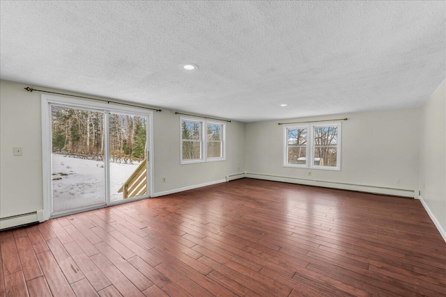 empty room with a textured ceiling, baseboard heating, wood finished floors, and baseboards