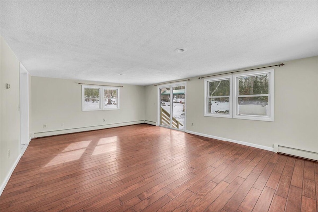 unfurnished room with a textured ceiling, baseboard heating, wood finished floors, and baseboards