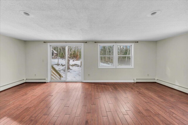 unfurnished room featuring a textured ceiling, a baseboard heating unit, wood finished floors, and baseboards