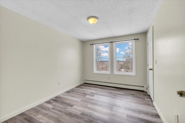 spare room with a textured ceiling, baseboard heating, wood finished floors, and baseboards