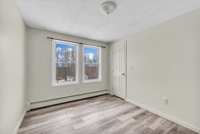 empty room with a baseboard heating unit, light wood-type flooring, a textured ceiling, and baseboards