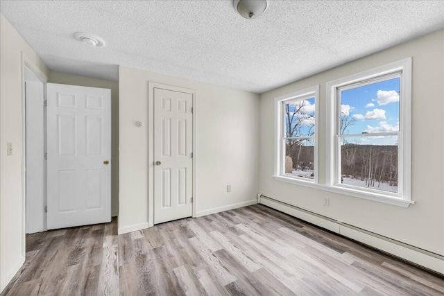 unfurnished bedroom featuring a baseboard heating unit, a closet, wood finished floors, and baseboards