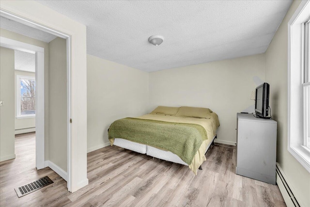 bedroom featuring a textured ceiling, wood finished floors, visible vents, baseboards, and baseboard heating