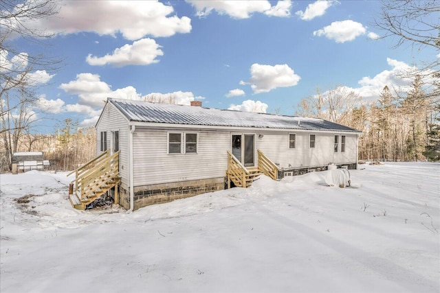 snow covered property featuring entry steps and metal roof