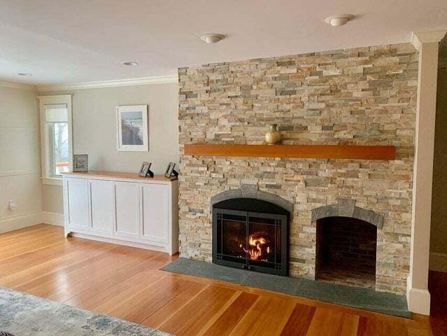 unfurnished living room featuring baseboards, a stone fireplace, wood finished floors, and crown molding