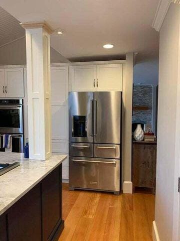 kitchen featuring stainless steel appliances, light wood-style flooring, white cabinets, light stone countertops, and ornate columns