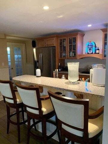 kitchen featuring glass insert cabinets, recessed lighting, refrigerator with ice dispenser, and a breakfast bar area