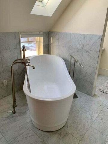 full bath with marble finish floor, lofted ceiling with skylight, a freestanding tub, and tile walls