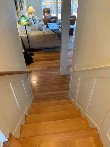 stairway with a wainscoted wall, a decorative wall, and wood finished floors