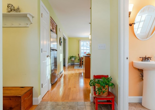 hallway featuring a baseboard radiator, baseboards, and a sink