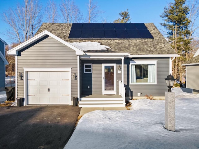 view of front facade with an attached garage, roof mounted solar panels, aphalt driveway, and roof with shingles