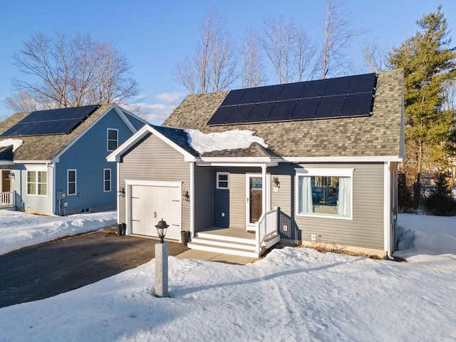 view of front of house featuring driveway, roof mounted solar panels, and roof with shingles