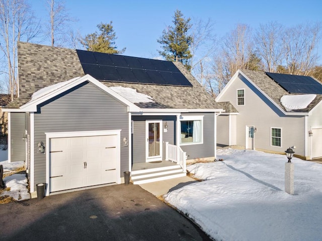 view of front of property with a garage, a shingled roof, roof mounted solar panels, and aphalt driveway