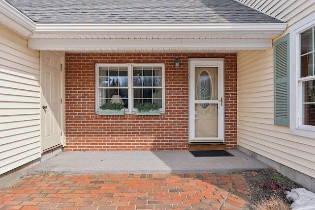 property entrance featuring brick siding and roof with shingles