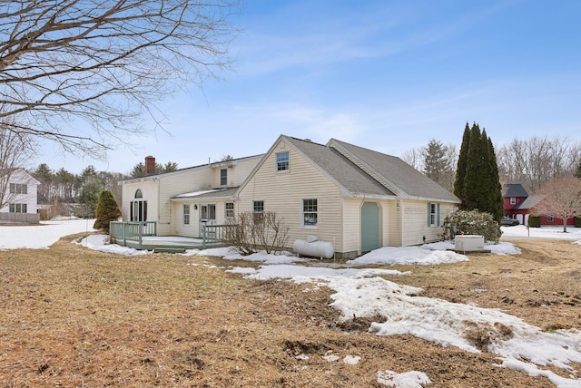 snow covered rear of property with a wooden deck and a chimney