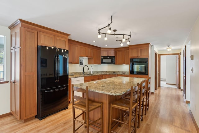 kitchen with brown cabinets, black appliances, light wood-style flooring, a sink, and light stone countertops