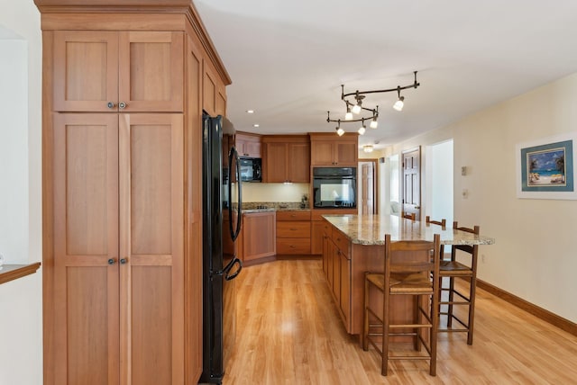 kitchen featuring a breakfast bar area, light stone counters, light wood finished floors, a kitchen island, and black appliances