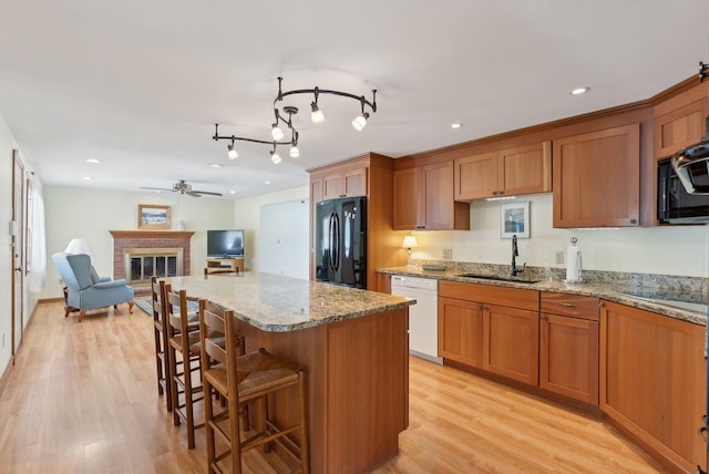 kitchen featuring a ceiling fan, light wood-style flooring, a sink, black appliances, and a brick fireplace