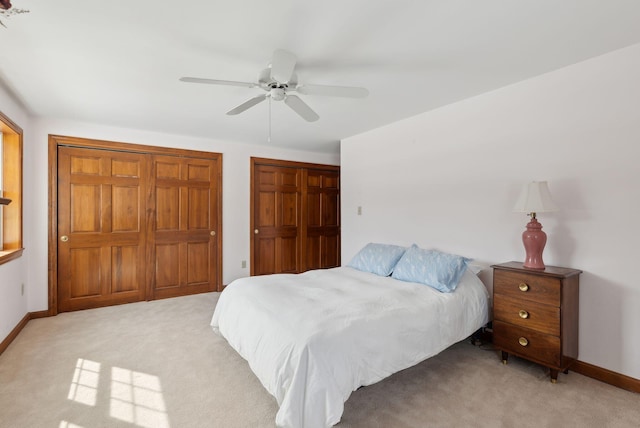 bedroom with light colored carpet, two closets, baseboards, and ceiling fan