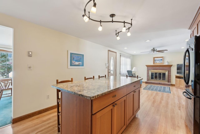 kitchen with a ceiling fan, baseboards, a breakfast bar, light wood-style flooring, and freestanding refrigerator