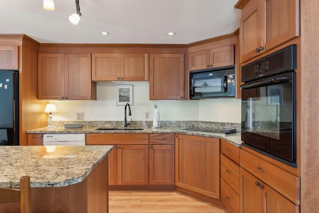 kitchen featuring brown cabinetry, black appliances, light stone counters, and a sink