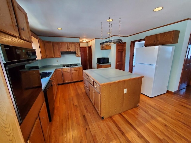 kitchen with light countertops, light wood-type flooring, a center island, black appliances, and crown molding